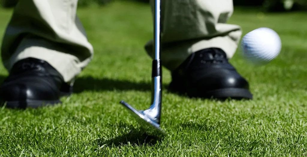 A golfer hitting the ball for a chip shot, ball and club in motion